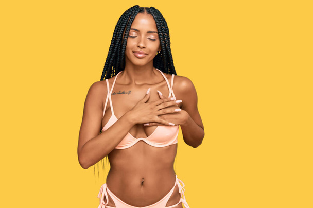 Beautiful hispanic woman wearing bikini smiling with hands on chest with closed eyes and grateful gesture on face. health concept.  - Foto, Imagen