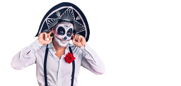 Man draagt dag van het dode kostuum over achtergrond lachende trekkende oren met vingers, grappig gebaar. auditieprobleem  - Foto, afbeelding