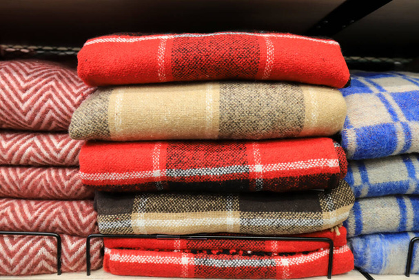 暖かく柔らかくふわふわしたウールのケージのプリッドのスタックは、ワードローブ、店の棚にあります。赤、青、冬の黄色のスーパーマーケットで暖かさと快適さのための毛布 - 写真・画像