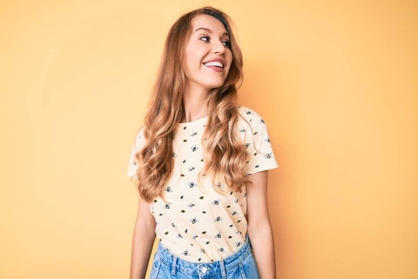 Молодая белая женщина с светлыми волосами в повседневной летней одежде, глядя в сторону, расслабиться профиль позировать с естественным лицом и уверенной улыбкой.  - Фото, изображение