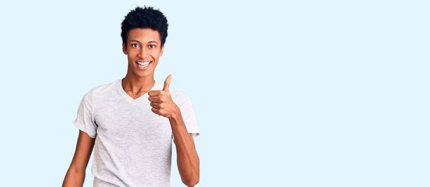 jovem afro-americano homem vestindo casual branco t-shirt sorrindo feliz e positivo, polegar-se fazendo excelente e sinal de aprovação  - Foto, Imagem