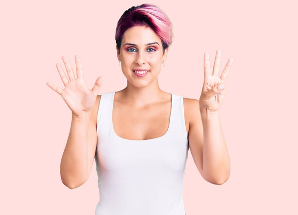 Молодая красивая женщина с розовыми волосами в повседневной одежде показывает и указывает пальцами номер восемь, улыбаясь уверенно и счастливо.  - Фото, изображение
