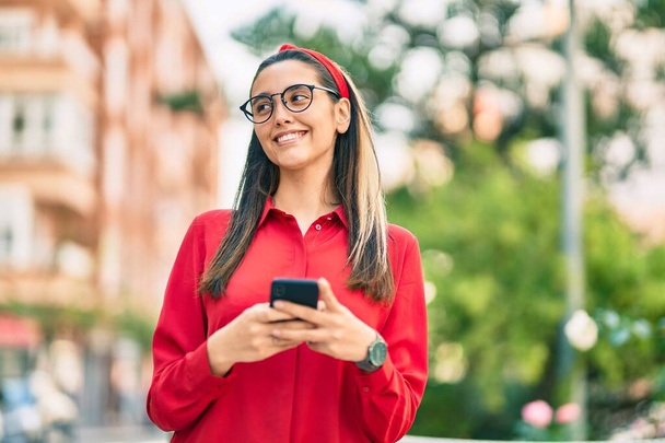 Joven mujer hispana sonriendo feliz usando smartphone en la ciudad. - Foto, imagen