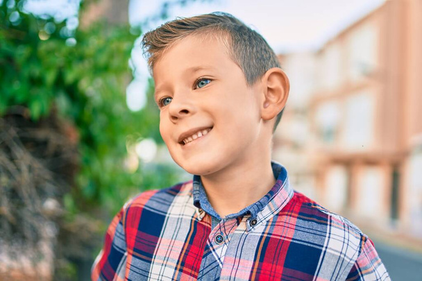 Αξιολάτρευτο καυκάσιο αγόρι χαμογελά χαρούμενος στέκεται στην πόλη. - Φωτογραφία, εικόνα