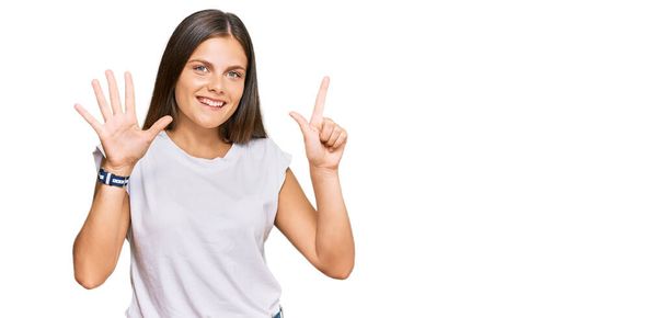 Mladá běloška na sobě ležérní bílé tričko ukazuje a ukazuje s prsty číslo sedm a zároveň se usmívá sebevědomě a šťastně.  - Fotografie, Obrázek