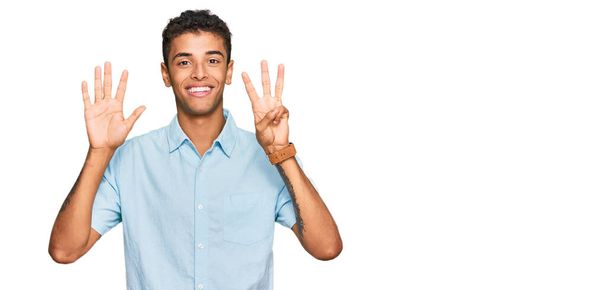Giovane bell'uomo afro-americano che indossa abiti casual mostrando e indicando con le dita il numero otto mentre sorride fiducioso e felice.  - Foto, immagini