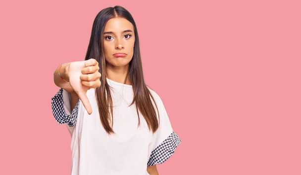 Young hispanic woman wearing casual clothes looking unhappy and angry showing rejection and negative with thumbs down gesture. bad expression.  - Fotografie, Obrázek