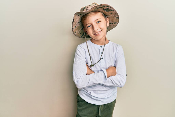Bonito garoto loiro vestindo chapéu de explorador sorrindo e olhando para a câmera apontando com duas mãos e dedos para o lado.  - Foto, Imagem