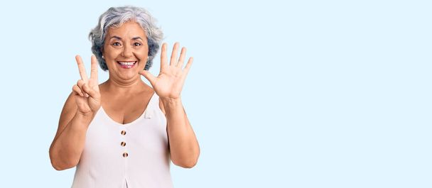 Starsza kobieta z siwymi włosami w luźnych ubraniach pokazuje i wskazuje palcem numer siedem, uśmiechając się z uśmiechem pewny siebie i szczęśliwy.  - Zdjęcie, obraz