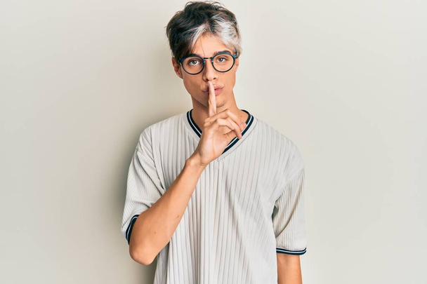 Jonge Latijns-Amerikaanse man in casual kleding en bril vraagt om stil te zijn met de vinger op de lippen. stilte en geheim concept.  - Foto, afbeelding