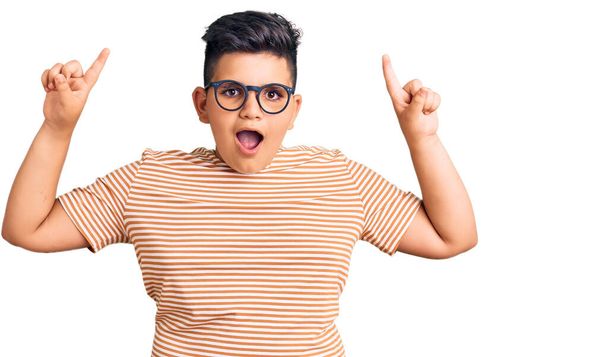Little boy kid wearing casual clothes and glasses smiling amazed and surprised and pointing up with fingers and raised arms.  - Photo, Image