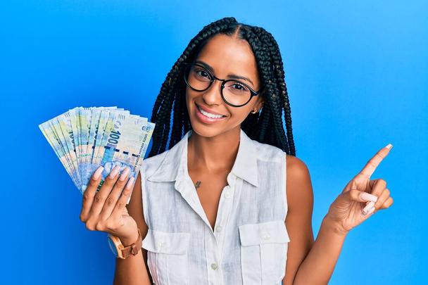 美しいhispic女性保持南アフリカ100ランド紙幣笑顔幸せなポインティングで手と指で側面  - 写真・画像