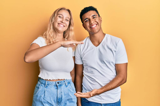 Молодая межрасовая пара в повседневной белой футболке жестикулирует руками, показывая большой и большой знак, измеряющий символ. улыбаясь, глядя в камеру. концепция измерения.  - Фото, изображение