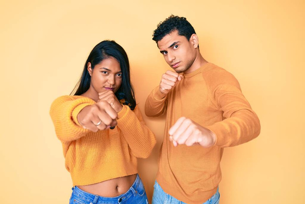 Hermosa pareja latina joven usando ropa casual juntos golpeando puño para luchar, ataque agresivo y enojado, amenaza y violencia  - Foto, imagen