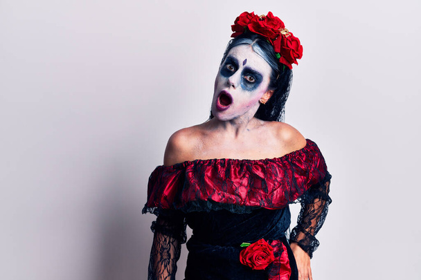 Jeune femme portant le jour mexicain du maquillage mort dans le visage de choc, l'air sceptique et sarcastique, surpris avec la bouche ouverte  - Photo, image