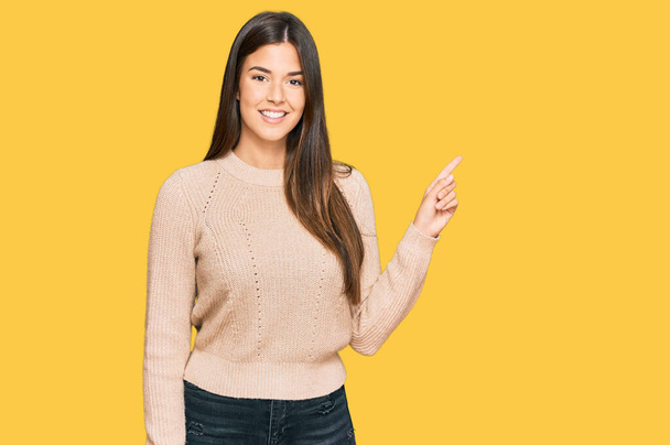 Young brunette woman wearing casual winter sweater with a big smile on face, pointing with hand finger to the side looking at the camera.  - Photo, Image