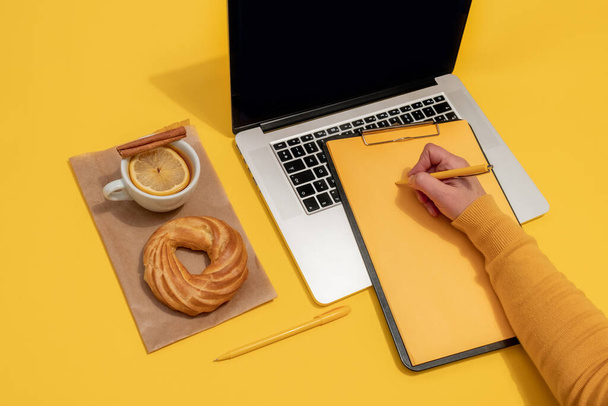 Hoja cerca de Laptop, pastel y taza de té en el fondo de color amarillo oro Fortuna, vista superior. - Foto, Imagen