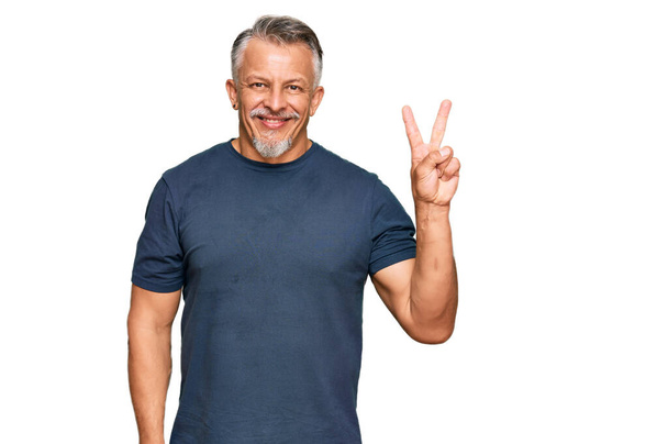 Hombre de pelo gris de mediana edad vistiendo ropa casual mostrando y señalando con los dedos número dos mientras sonríe confiado y feliz.  - Foto, imagen