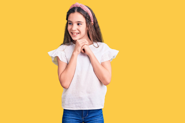 Χαριτωμένο ισπανόφωνο κορίτσι φορώντας casual λευκό μπλουζάκι γελώντας νευρικό και ενθουσιασμένο με τα χέρια στο πηγούνι κοιτάζοντας στο πλάι  - Φωτογραφία, εικόνα