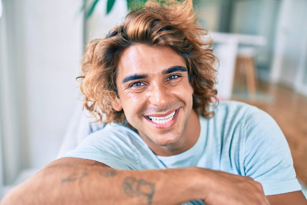 Jovem hispânico sorrindo feliz sentado no sofá em casa - Foto, Imagem
