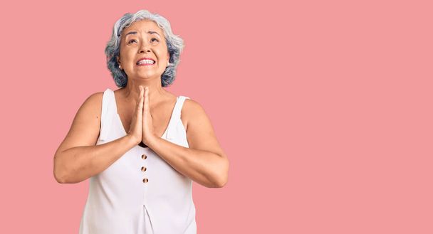 Oudere vrouw met grijs haar in casual kleding bedelen en bidden met de handen samen met hoop uitdrukking op het gezicht zeer emotioneel en bezorgd. bedelen.  - Foto, afbeelding