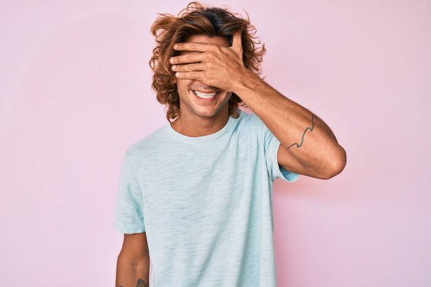 Young hispanic man wearing casual clothes smiling and laughing with hand on face covering eyes for surprise. blind concept.  - Photo, Image