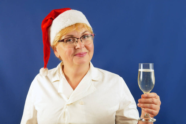 kobieta lekarz świętujący ferie zimowe w pracy w mundurze i Santa Claus kapelusze z kieliszkiem szampana. Bogactwo i zdrowie w koncepcji nowego roku. Wesołych Świąt i Szczęśliwego Nowego Roku! Zbliżenie - Zdjęcie, obraz