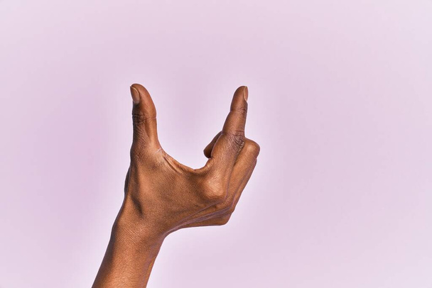 Arm and hand of black middle age woman over pink isolated background picking and taking invisible thing, holding object with fingers showing space  - Zdjęcie, obraz