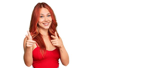 幸せと面白い顔でカメラに指を指してカジュアルな服を着て若い赤毛の女性。良いエネルギーと振動は.  - 写真・画像
