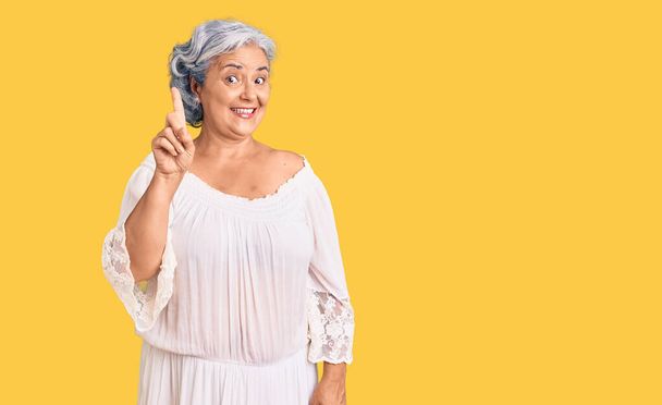 Seniorin mit grauen Haaren im Bohème-Stil zeigt mit erhobenem Zeigefinger auf erfolgreiche Idee. aufgeregt und glücklich. Nummer eins.  - Foto, Bild