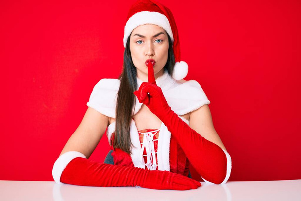 Young caucasian woman wearing santa claus costume asking to be quiet with finger on lips. silence and secret concept.  - Photo, Image