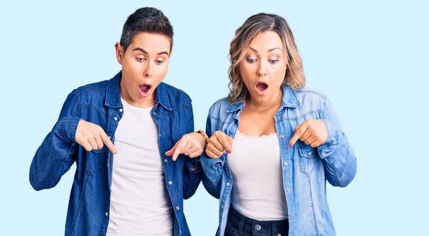 Couple de femmes portant des vêtements décontractés pointant vers le bas avec les doigts montrant la publicité, visage surpris et bouche ouverte  - Photo, image