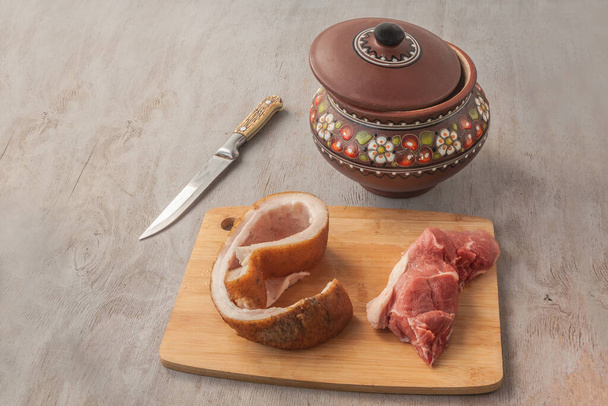 Trozo de cerdo en una tabla de cortar sobre el fondo de la olla (producto producido en masa) con una tapa en la mesa de la cocina. Borscht de cocina. - Foto, Imagen