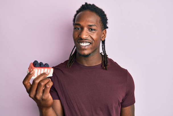 自信を持って笑顔で歯を示す正と幸せな立ちと笑顔を見てチーズケーキプレートを保持アフリカ系アメリカ人男性  - 写真・画像