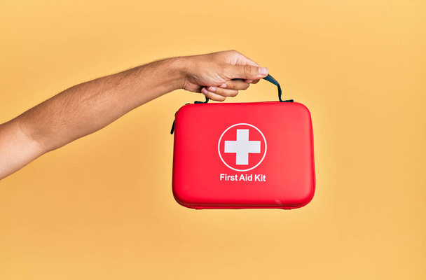 Hand of hispanic man holding first aid kit over isolated yellow background. - Photo, Image