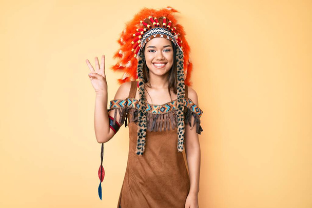 Mladý krásný latinsky dívka na sobě indický kostým ukazuje a ukazuje s prsty číslo tři a zároveň se usmívá sebevědomě a šťastně.  - Fotografie, Obrázek