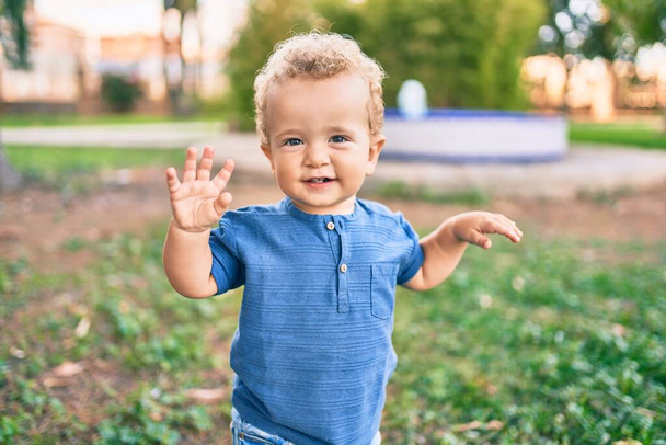 Милый и счастливый маленький мальчик веселится в парке в солнечный день. Красивые светлые волосы мужчина ребенок играет на открытом воздухе - Фото, изображение
