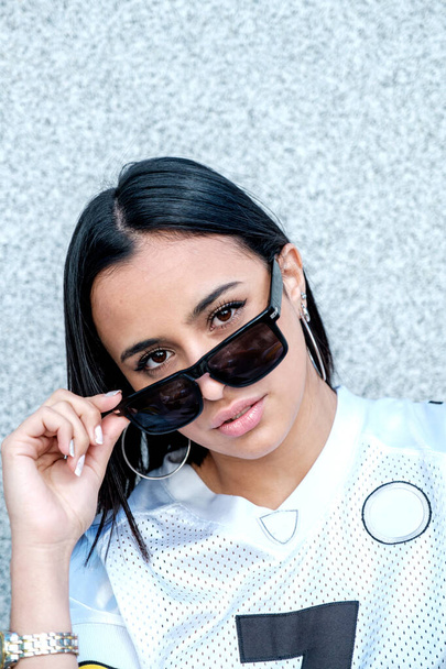 A closeup vertical portrait of a sporty Hispanic woman in stylish sunglasses posing outdoors - Фото, зображення