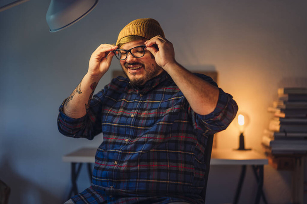 A closeup portrait of a young smiling man putting his optical glasses on while being at home - Foto, imagen