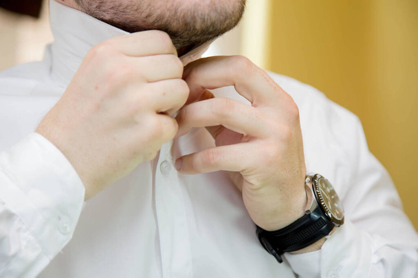 A closeup of the groom buttoning the last button of his shirt on his wedding day - Foto, imagen