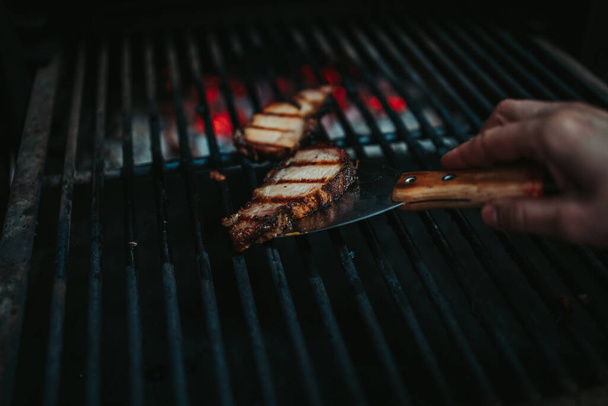 a hand taking the grilled meat out of the oven with a kitchen tool - Foto, afbeelding