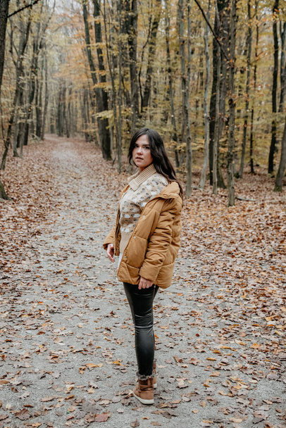 A vertical shot of a beautiful Caucasian woman having a walk in the woods during autumn - Photo, image