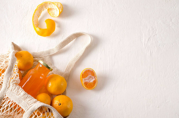 Getränk aus Mandarinen in der Flasche und Mandarinenfrüchte liegen in einem Netzbeutel auf hellem Hintergrund mit Kopierraum, selektiver Fokus, horizontaler Hintergrund - Foto, Bild