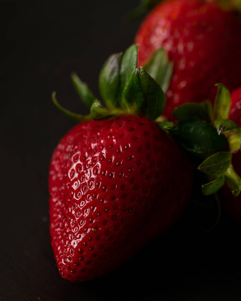 A vertical shot of a ripe delicious strawberry against a dark blurry background - Zdjęcie, obraz
