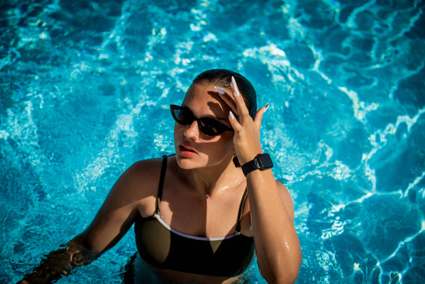 Modeporträt eines anmutigen netten Mädchens mit stylischer Sonnenbrille, das während des Urlaubs im Luxus-Resort im Pool posiert. Fröhlich plus Größe Teenager Mädchen genießen. glücklich, positive Emotion, sommerlicher Stil. - Foto, Bild
