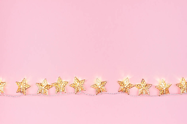 Festive golden stars glowing lights on soft light pink background, copy space, top view. - Fotó, kép