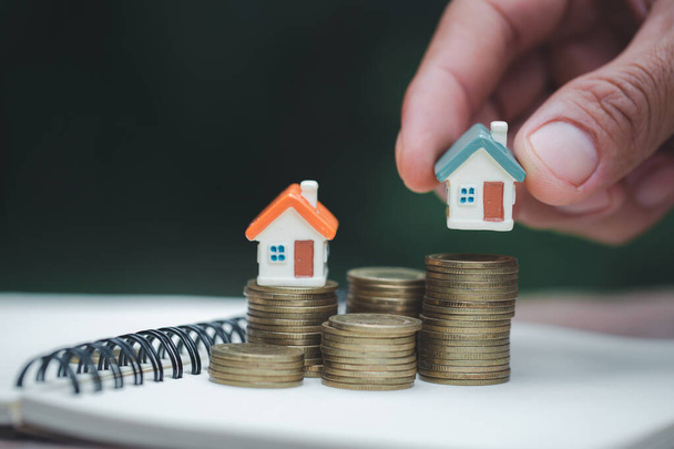 Eine Frau, die ein Haus auf einem Haufen Münzen hält, plant Ersparnisse. Konzept für Immobilien-, Hypotheken- und Immobilieninvestitionen. zum Sparen oder Investieren in ein Haus. - Foto, Bild