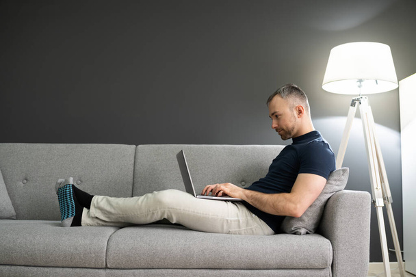 Man Sitting In Sofa At Home And Using Laptop - Foto, afbeelding