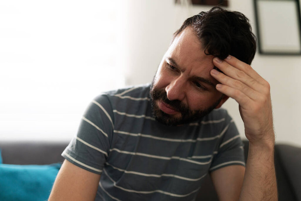 Latin adult man sitting on the sofa with one hand in his forehead and looking worried and stressed in his home - Photo, Image