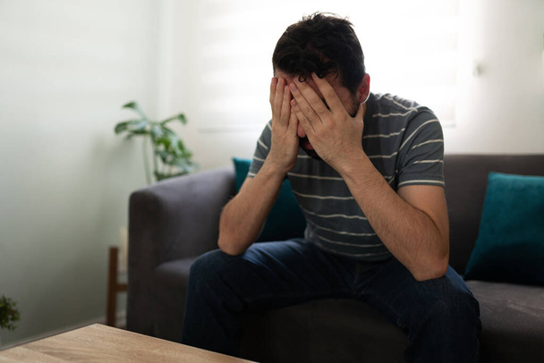 Hispanic man covering his face with his hands, looking sad and depressed on the couch - Photo, Image